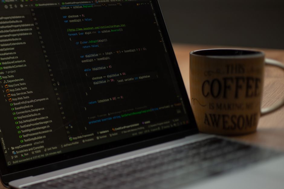 Code on a dark laptop screen beside a coffee mug